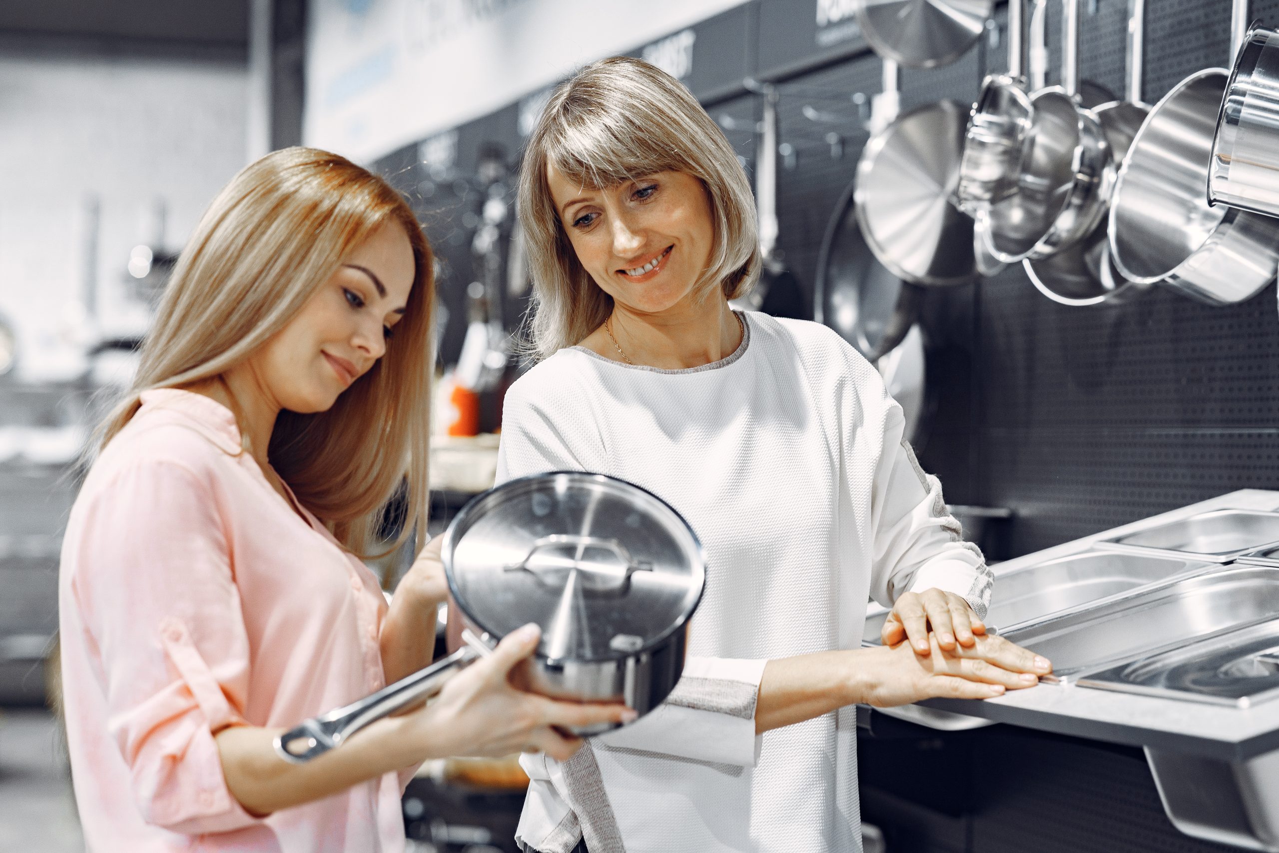 Woman examines various items of dishes. Beautiful woman shopping tableware in supermarket. Manager helps a costumer.
